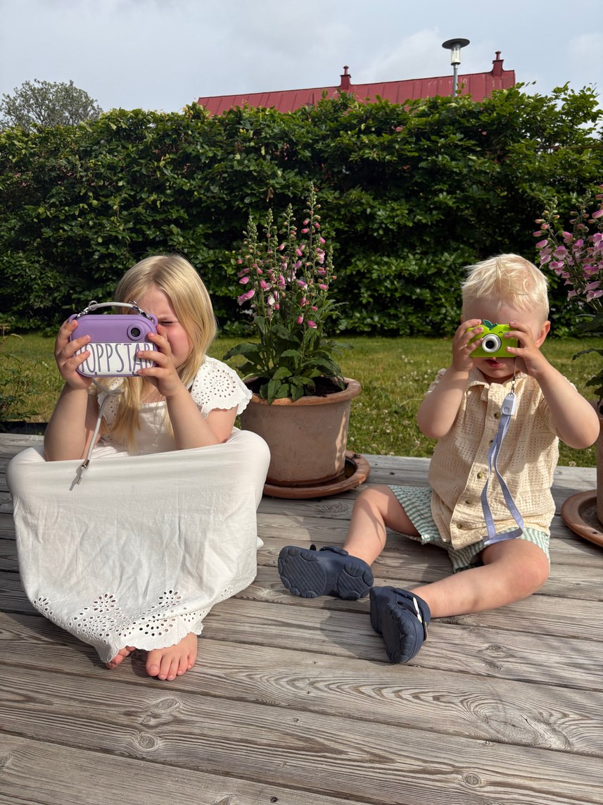 Two children playing with toy cameras on a wooden deck
